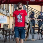 Фотография мужчины, идущего по улице в красной футболке. На его предплечье видна татуировка в черно-серых тонах, изображающая сложный узор.