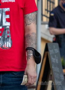 Крупный план татуировки на предплечье мужчины, выполненной в черно-серых тонах. Видны сложные узоры и детализированные элементы рисунка.
