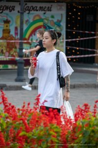 Фотография девушки с татуировкой на предплечье, идущей по городской улице. Татуировка выполнена в темных тонах и имеет сложный узор.