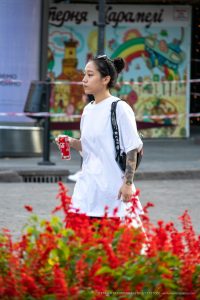 Фотография девушки с татуировкой на предплечье, идущей по городской улице. Татуировка выполнена в темных тонах и имеет сложный узор.