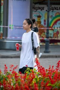 Фотография девушки с татуировкой на предплечье, идущей по городской улице. Татуировка выполнена в темных тонах и имеет сложный узор.