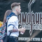 Фотография мужчины с татуировкой на руке, стоящего на фоне яркого граффити. Рисунок татуировки выполнен в темных тонах, с деталями и контурами.