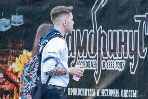 Фотография мужчины с татуировкой на руке, стоящего на фоне яркого граффити. Рисунок татуировки выполнен в темных тонах, с деталями и контурами.