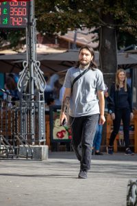 Фотография мужчины с татуировкой на руке, идущего по улице. Рисунок татуировки выполнен в черных тонах, с изображением обезьяны, показывающей знак 'рок'.