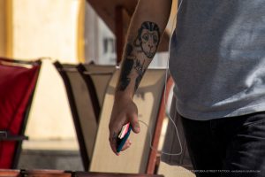 Фотография татуировки обезьяны на руке мужчины. Рисунок татуировки выполнен в черных тонах, с изображением обезьяны, показывающей знак 'рок'.