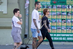 Фотография с изображением татуировок на ногах и руках у двух прохожих. Видны детализированные рисунки в различных стилях.