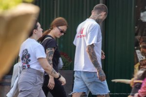 Фотография с изображением татуировок на руках и ногах у двух прохожих. Видны детализированные рисунки в различных стилях, включая традиционные и графические.
