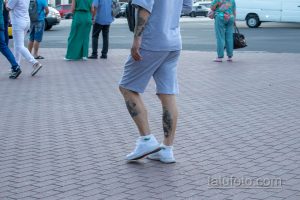 Фото тату на теле мужчины: рисунки на ноге и руке, выполненные в черном цвете. Видны детализированные узоры и символы.