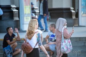 Фотография девушки с акварельной татуировкой на руке. Татуировка изображает цветы и маску, выполнена в ярких цветах. Девушка спускается по лестнице.