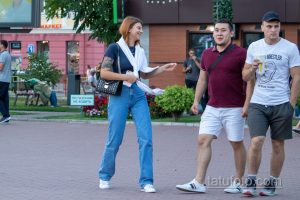Фотография трех людей на улице, у девушки на руке видна красочная татуировка с цветами и маской. Летний день, городская среда.