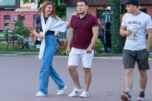 Фотография трех людей, гуляющих по улице. У девушки на левой руке видна татуировка с цветами. Яркий летний день.