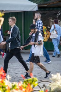 Фото мужчины с татуировкой на руке, идущего по улице с рюкзаком. Вид сбоку, солнечный день.