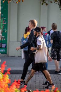 Фото татуировки на руке мужчины, идущего по улице с другом. Вид сбоку, солнечный день.
