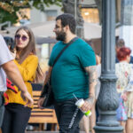 Фото мужчины с татуировкой на предплечье и женщины с собакой породы такса. Детализированный рисунок татуировки в стиле олдскул.