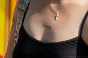 Фото тату: маленькая надпись 'Strong' черными чернилами на женской груди. Минималистичный стиль, тонкие линии, нежная кожа.