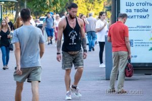 Фотография мужчины с татуировкой на руке, идущего по улице. Татуировка выполнена в темных тонах и занимает большую часть предплечья.