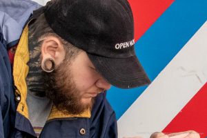 Фото татуировки: черно-белый рисунок на шее мужчины, выполненный в графическом стиле. Изображение напоминает ветви дерева или корни.