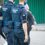 Фото тату: сотрудник Национальной гвардии Украины с черной татуировкой-надписью на предплечье и нашивкой флага Украины.
