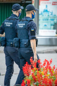 Фото тату: сотрудник Национальной гвардии Украины с черной татуировкой-надписью на предплечье и нашивкой флага Украины.