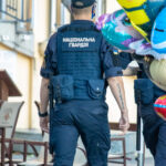 Фото тату: сотрудник Национальной гвардии Украины с черной татуировкой-надписью на предплечье на фоне ярких воздушных шаров.
