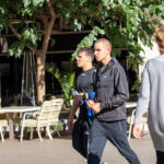 Фотография мужчины с татуировкой на руке, идущего по улице в компании двух других людей. Видна часть татуировки на предплечье.