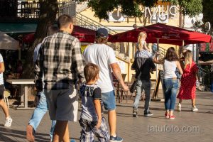 Фото тату: мужчина с татуировкой на предплечье, идущий в толпе людей на улице. Татуировка выполнена в черных тонах.