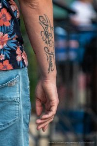 Фото татуировки на руке мужчины, представляющей собой надпись, выполненную в стиле каллиграфии. Черные чернила, изящный шрифт.
