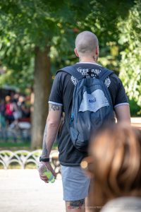 Фото тату на теле мужчины: татуировки на шее, предплечье и ногах, выполненные в разных стилях. Мужчина с рюкзаком на улице.