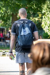 Фото тату на теле мужчины: татуировки на шее, предплечье и ногах, выполненные в разных стилях. Мужчина с рюкзаком на улице.