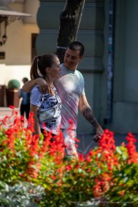 Фото пары: мужчина с татуировкой на предплечье и женщина с татуировкой на плече, стоящие на фоне ярких красных цветов.
