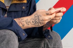 Фото тату: татуировка осьминога на руке мужчины. Черно-белый рисунок татуировки, детализированный и стильный. Фотография сделана в интерьере.