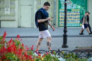 Фото тату на ногах и руках мужчины, идущего по улице. Видны надписи и небольшие рисунки, выполненные в черном цвете. Уличная татуировка.