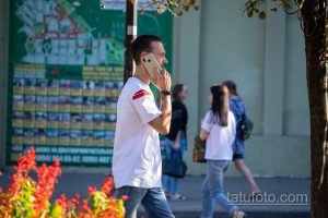 Фото мужчины с татуировками на предплечье, разговаривающего по телефону. Видны детализированные рисунки татуировок в различных стилях.