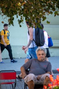 Фотография мужчины с татуировкой волка на руке, идущего по улице. Тату выполнено в реалистичном стиле и занимает большую часть предплечья.