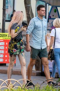Фото девушки с татуировками на руках и ногах. На руках видны рисунки в виде змей и цветов, на ногах - детализированные татуировки. Стильные татуировки дополняют образ.
