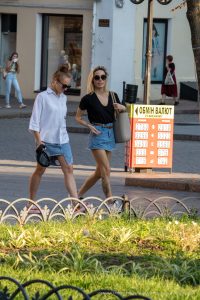Фото двух девушек с татуировками на ногах. Одна девушка в белом платье, другая в джинсовых шортах и футболке. Стильные татуировки дополняют летние образы.