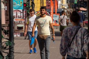 Фото тату на предплечье мужчины, идущего по улице. Рисунок татуировки выполнен в темных тонах, с преобладанием черного цвета. Видны детализированные узоры.