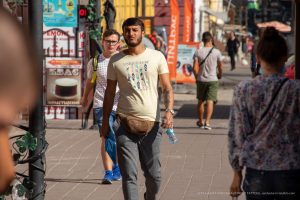Фотография мужчины с татуировкой на руке, идущего по улице. Татуировка выполнена в темных тонах, изображает пальмы.