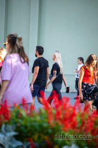 Фотография пары, идущей по улице, у девушки на руке видна татуировка, а мужчина держит ее за руку.
