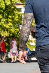 Фото тату на руке: крупный план татуировки с изображением виноградной лозы, гроздей и листьев в черно-серых тонах. Детальный рисунок.