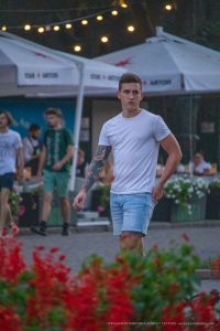 Фото тату на руке молодого человека, идущего по улице. Татуировка выполнена в темных тонах, изображает абстрактный рисунок.