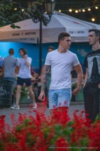 Фотография мужчины с татуировкой на руке, идущего по улице. Татуировка выполнена в темных тонах и занимает большую часть предплечья.