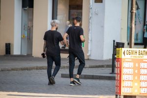 Фотография двух мужчин, идущих по улице, с видимыми татуировками на руках. Один из мужчин с седыми волосами, оба одеты в черное.