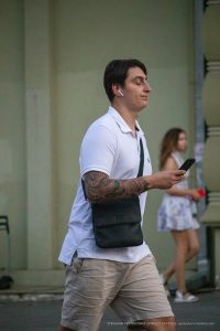 Фотография мужчины с татуировкой на предплечье, смотрящего вдаль. Он одет в белую футболку и шорты, в ушах наушники.