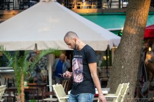 Фото мужчины с татуировками на руках, шее и плечах, в черной футболке, уличный стиль, портретная татуировка.