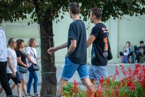Фотография двух мужчин, идущих по улице, с видимыми татуировками на руках. Летний день, городская сцена.