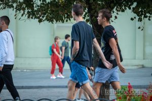 Фотография двух мужчин, идущих по улице, с видимыми татуировками на руках. Летний день, городская сцена.
