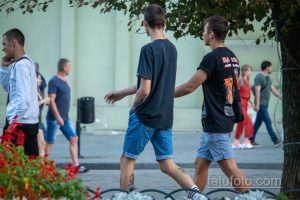 Фотография двух мужчин, идущих по улице, с видимыми татуировками на руках. Летний день, городская сцена.