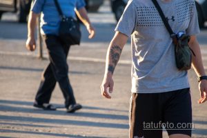 Фото тату: мужчина с татуировкой в виде индейского вождя на руке, идущий по улице.
