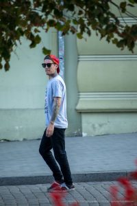 Фото мужчины с татуировками на руках, шее и плечах, в кепке и очках, уличный стиль.